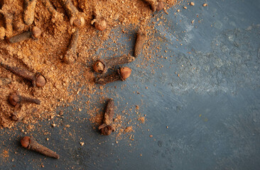 Fresh whole and ground clove spice on a dark blue backdrop, evoking winter warmth.