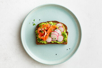 Avocado toasts with salmon, radish, and herbs on a plate. Healthy breakfast. Copy space.