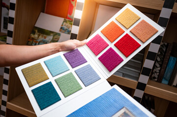 Designer hand holding carpet fabric swatch collection. Customer choosing color sample from rug...