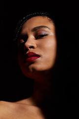 A fashionable young woman confidently poses with braided hair and striking red lips in a studio atmosphere.