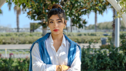 A young brunette businesswoman in a park full of trees on a spring day looks at the camera with facial expressions showing she is sad