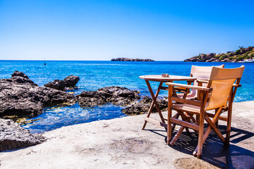 Fototapeta premium Chairs and table in a restaurant with a view of a sea in the background , Scenic view , Loutro village , Greece
