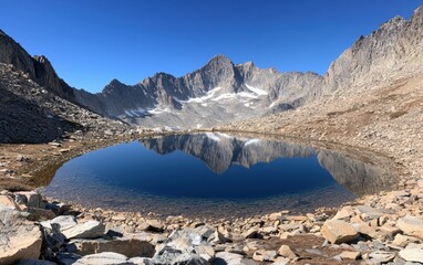 Obraz premium A serene alpine lake nestled between rugged mountains, reflecting the clear sky above