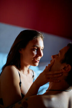 Smiling woman affectionately touching the face of her boyfriend in a dimly lit room.