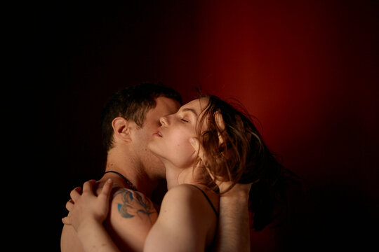An intimate moment between a couple as they embrace and kiss, illuminated by soft, warm light against a dark backdrop.