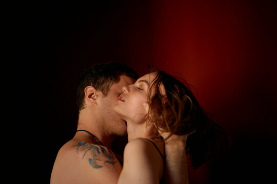 Close-up of a man and woman embracing and kissing against a dark background with warm lighting.