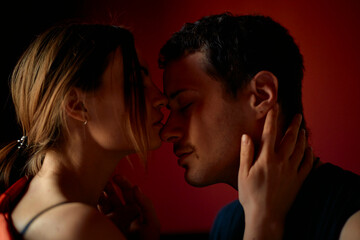 Silhouetted couple about to kiss, illuminated by a soft red light in a romantic setting.