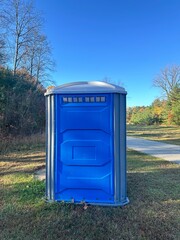 Blue porta potty outdoor bathroom in the park during colorful autumn