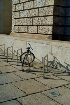 A single bicycle locked to a metal bike rack casting a long shadow on a sunny day near a stone wall, Berlin, Germany
