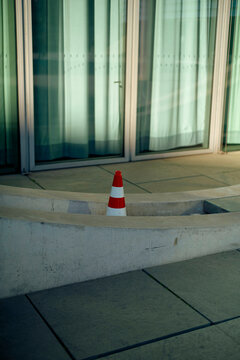 Red and white traffic cone sits on a concrete ledge in front of a glass building, Berlin, Germany