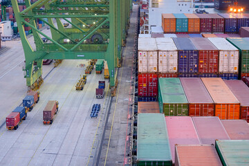Elevated view of a busy container terminal with stacked colorful containers and operational cargo trucks during twilight, Singapore