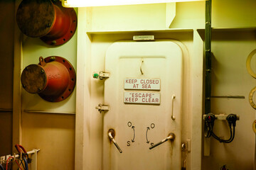 Watertight door on a ship with safety instructions reading KEEP CLOSED AT SEA and ESCAPE to ensure security and emergency awareness.