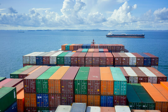 Aerial view of colorful shipping containers stacked on a cargo ship with an expansive ocean and a cloudy sky in the background.