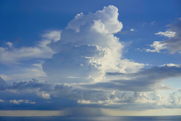 Majestic cumulus cloud towering over a serene sea under a blue sky with soft light piercing through, South China Sea