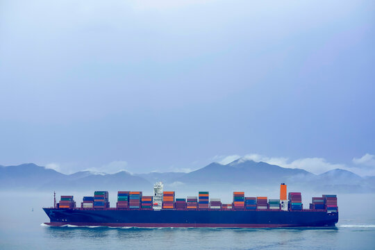 A large Hapag-Lloyd cargo ship filled with containers sails on the sea against a backdrop of hazy mountains, Busan, Korea