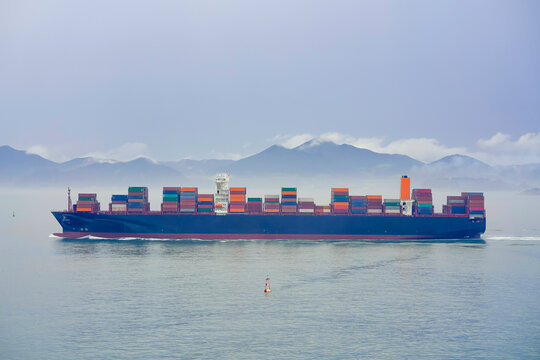 Cargo ship sailing on a foggy ocean with a tranquil mountain backdrop, Busan, Korea