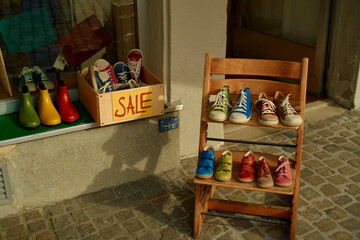 Colorful shoes on sale displayed outside a shop on a sunny day, with pairs neatly arranged on a wooden chair and in a box.