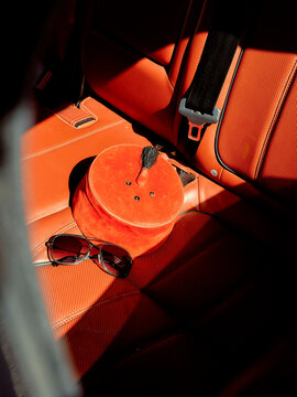 Orange velvet hat box and sunglasses resting on a red leather car seat bathed in sunlight, Morocco