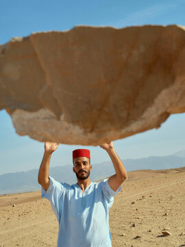 A man in traditional attire throwing a piece of fabric above his head in a desert landscape, Morocco