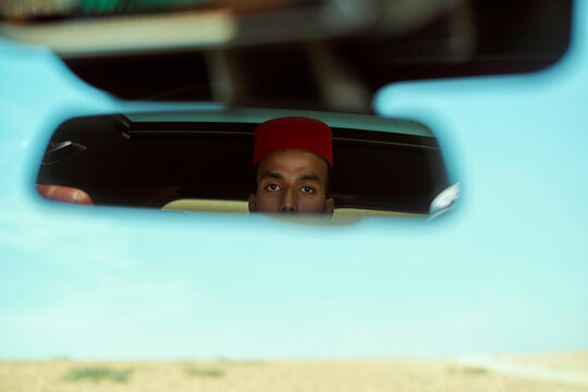 Man with red cap reflected in rearview mirror of a car, Morocco