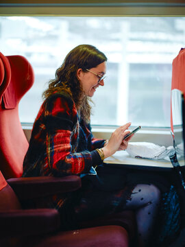 Smiling woman using a smartphone while seated in a train compartment with red seats.
