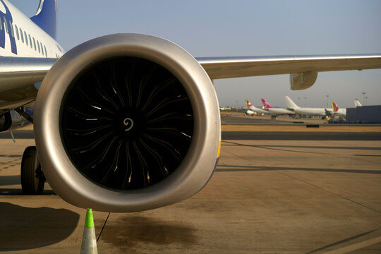 Close-up view of a jet engine on an airplane at an airport with other planes in the background on a clear day.