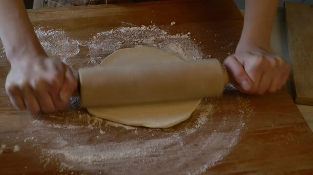 woman in an apron rolling out dough with a rolling pin to make dumplings in her kitchen