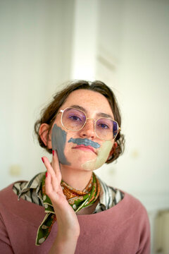 A confident young woman with artistic paint gazes directly at the camera, sporting a casual yet fashionable outfit.