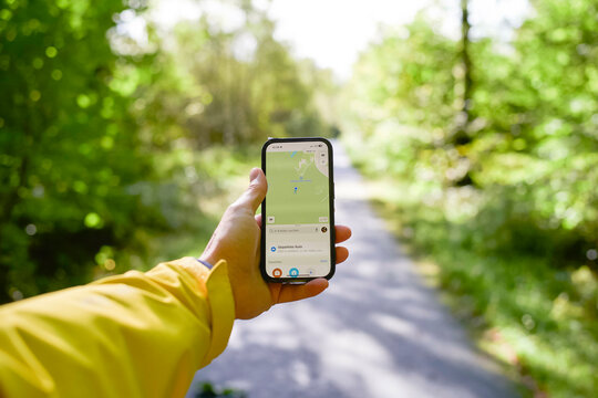 Hand holding a smartphone with a navigation map on the screen in a lush green forest setting.