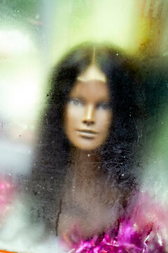 Scary female puppet head seen through the steamy window of a shop display