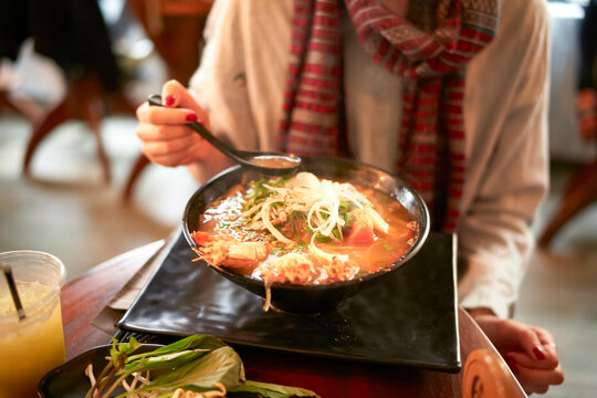 Close-up of a person dining at a restaurant, enjoying a steaming bowl of Asian noodle soup.