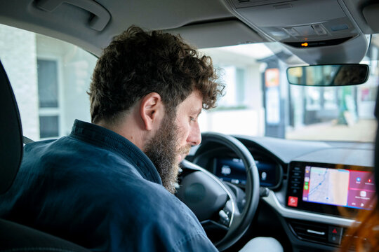 Man with curly hair driving a car, looking at the road ahead with a navigation system on the dashboard.