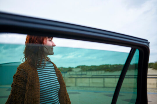 Side view of a smiling woman in a striped shirt seen through a car window with a clear sky in the background.