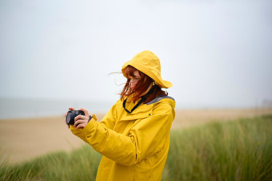 Woman in yellow raincoat checking her camera on a cloudy beach day, Belgium