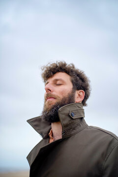 Close-up of a bearded man with his eyes closed, breathing in outdoor air, wearing a brown jacket, Belgium