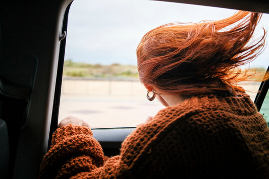 Woman with red hair in a brown sweater looks out the car window on a windy day, Belgium