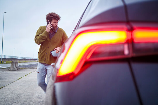 Man with curly hair walking past a car while talking on the phone, Belgium