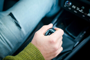 Close-up of a person's hand shifting a car's gear stick while driving.