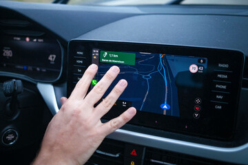Hand interacting with a car's touchscreen navigation system showing a map and various control options.