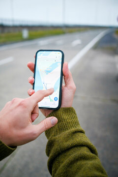 A person uses a smartphone with a navigation app on the screen, holding the phone in one hand and interacting with the touchscreen