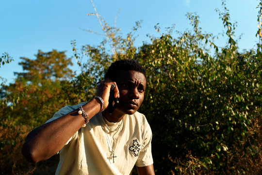 A focused man outdoors making a phone call during golden hour with foliage in the background, Berlin, Germany