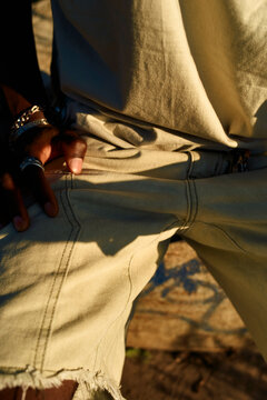 Close-up of a person's hand on the pocket of distressed denim jeans, adorned with a silver ring, bathed in warm sunlight, Berlin, Germany