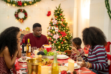 A cheerful holiday dinner scene with a diverse family enjoying a festive meal. Christmas decorations, gifts, and a lit Christmas tree create a cozy atmosphere, enhancing the warmth of the celebration.