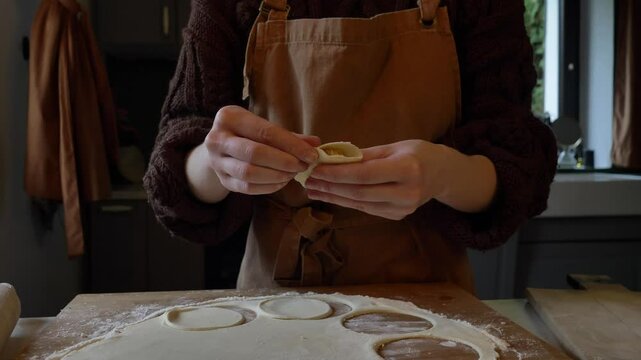 woman in an apron making dumplings with dough and cabbage at her table at home