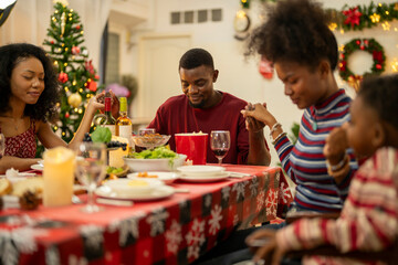 A warm Christmas family dinner with a father serving food to his young child, surrounded by festive decorations, a Christmas tree, and a holiday table spread. Joyful and cozy holiday atmosphere.