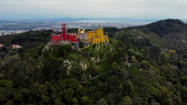 Famous National Palace of Pena situated in Sintra, Portugal. Drone descending. City of Sintra and Lisbon in background. Famous travel destination. The palace is a UNESCO World Heritage Site. 
