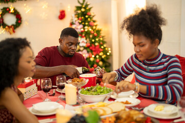 A family enjoys a festive Christmas dinner, sharing food and creating memories. A beautifully decorated Christmas tree and wreath add warmth, while candles and decor enhance the cozy holiday setting.