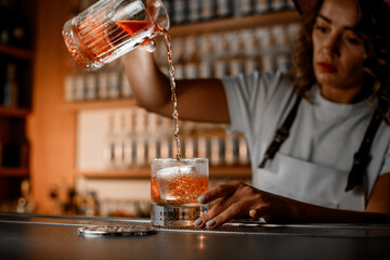 Focus on the process of pouring the finished brown cocktail from a mixing glass