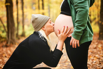 Lesbian couple having fun on autumn forest with futur newborn child on woman belly.