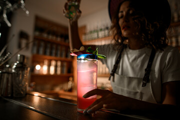 Tall glass with a pink drink, illuminated by a light stands on the bar counter